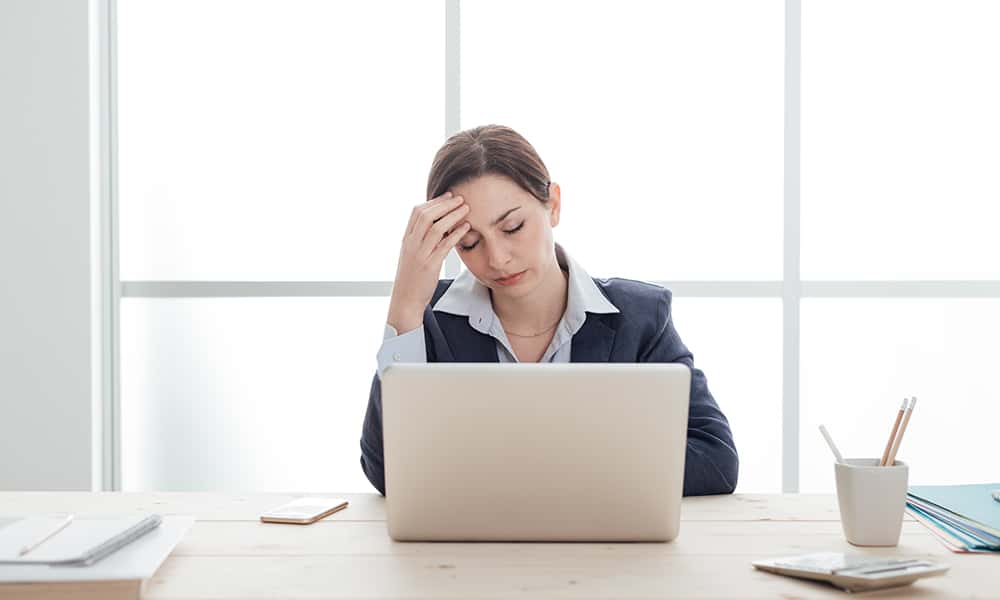 The image shows a woman, office worker suffering from a headache