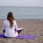 person cross legged on a yoga mat at the beach