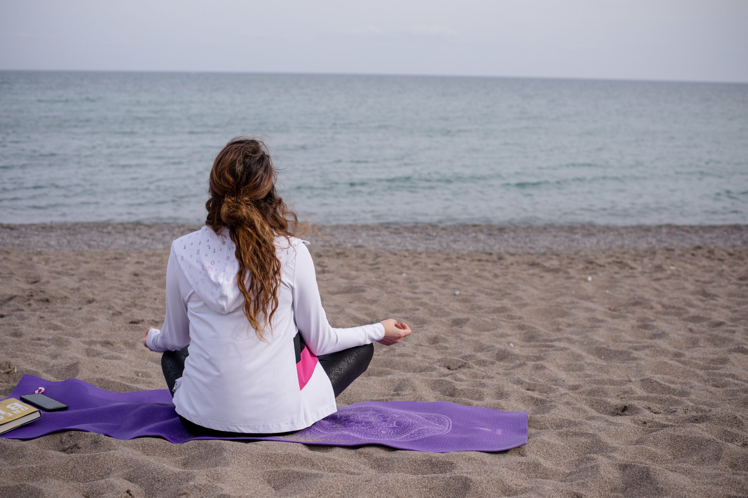 person cross legged on a yoga mat at the beach scaled