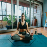woman smiles wide sitting cross legged on yoga mat