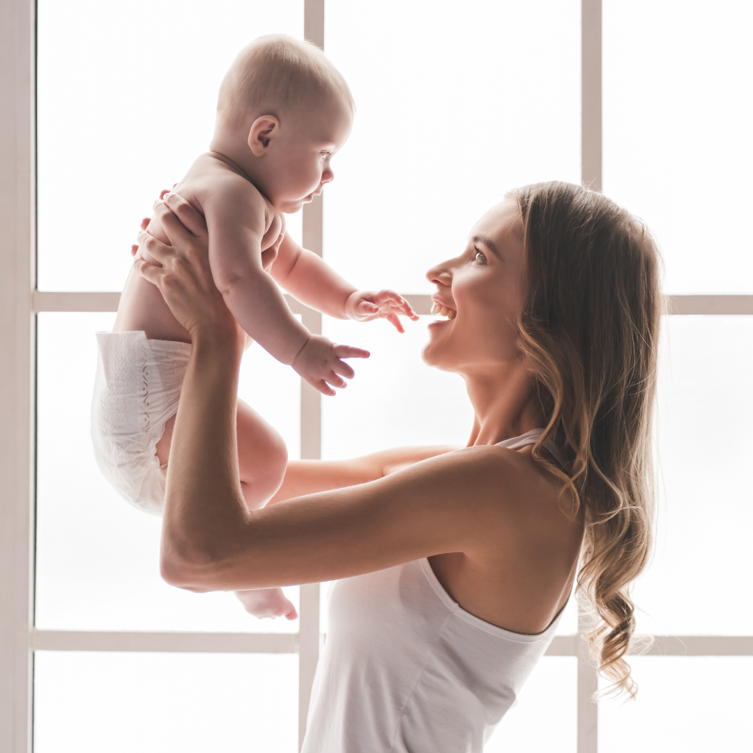 Young mother smiling holding her baby by the window