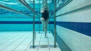 Woman doing hydrotherapy in the pool and walking holding on to bars.