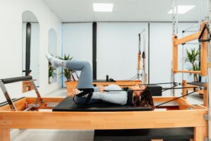 Person exercising on a Pilates reformer machine in a fitness studio.