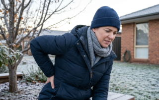 Woman wincing with a stiff, sore back while getting up from a frosty garden bench.